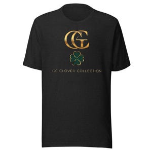 May include: A dark gray t-shirt featuring a gold-colored "GC" logo above a green shamrock. The text "GC CLOVER COLLECTION" is printed below the shamrock in a simple font. The shirt has short sleeves and a crew neck.