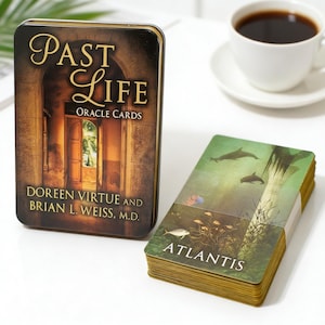 May include: A rectangular metal tin featuring the text Past Life Oracle Cards by Doreen Virtue and Brian L. Weiss, M.D. next to a deck of cards with an Atlantis illustration showing dolphins and underwater plants with gold-toned card edges.
