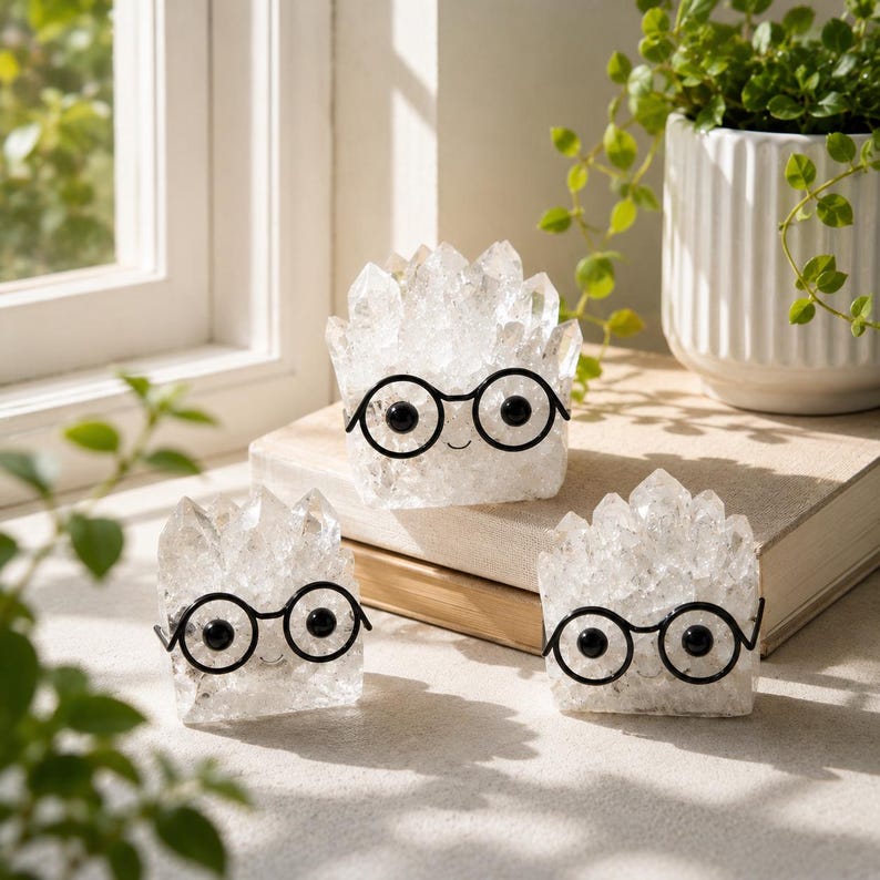 May include: Three clear, jagged quartz crystal clusters shaped like small figures, each featuring a pair of black wire-rimmed glasses with round frames and small black circular eyes, creating a character-like appearance on each crystal.