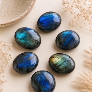 May include: Six polished, oval-shaped labradorite stones arranged in a circular pattern. Each stone features a dark gray base with iridescent flashes of vibrant blue, teal, and gold light reflecting from within the smooth, reflective surfaces.