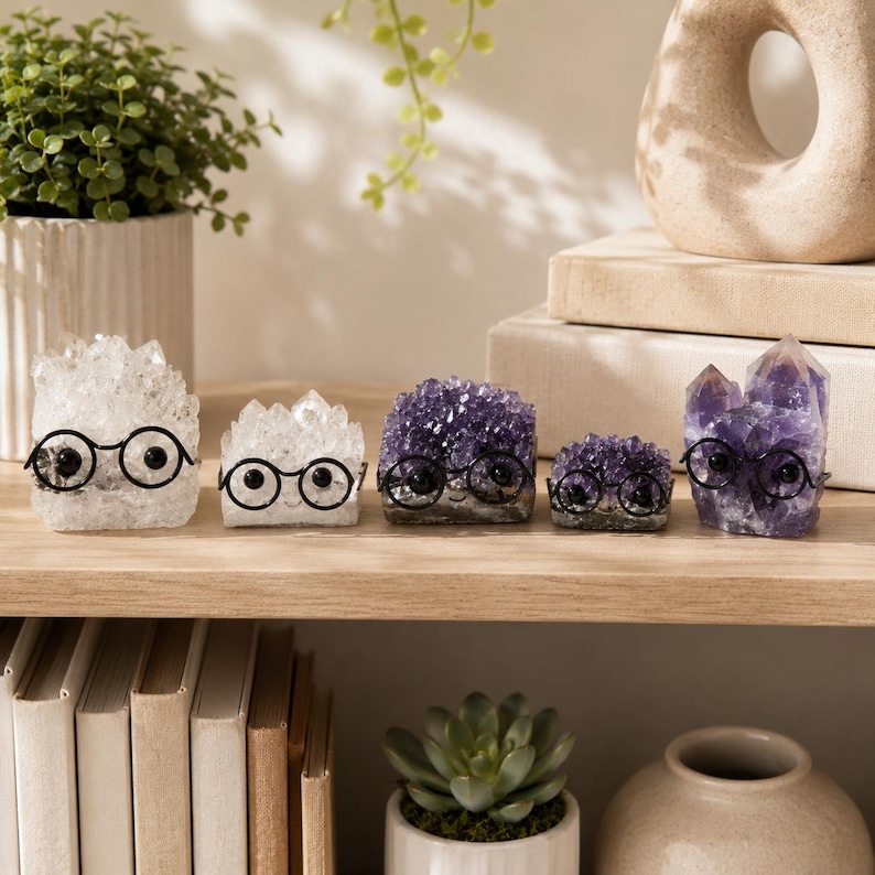 May include: Five crystal clusters arranged in a row, each featuring a pair of small black wire-rimmed glasses. The collection includes two clear quartz clusters and three purple amethyst clusters, all displaying natural jagged crystalline structures.