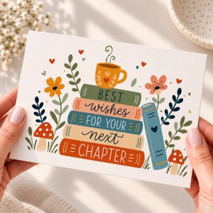 May include: A rectangular greeting card featuring a stack of four colorful books topped with a steaming orange mug. The text reads BEST WISHES FOR YOUR NEXT CHAPTER. The design includes orange and pink flowers, red mushrooms, and small hearts.