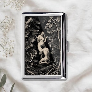 May include: A rectangular silver metal cigarette case featuring a black and white engraved illustration of two figures in a forest setting. The artwork depicts a standing figure and a kneeling figure surrounded by detailed trees and foliage.
