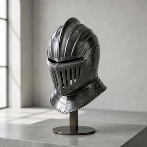 Puede incluir: Un yelmo de caballero medieval gris oscuro con visera y protector de cuello, expuesto sobre un soporte de bronce. El yelmo presenta detalles remachados y una parte superior acanalada, mostrando la artesanía histórica. Símbolo de protección y valor.