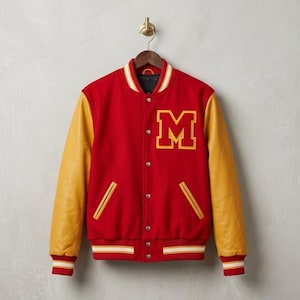 Puede incluir: Chaqueta universitaria roja y dorada con la letra "M" en el pecho. La chaqueta tiene mangas de cuero doradas, un dobladillo y puños acanalados con rayas blancas y rojas, y una parte delantera abotonada. La chaqueta está colgada de una percha de madera.