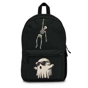 Könnte beinhalten: Ein schwarzer Rucksack mit einer weißen Grafik eines Skeletts, das einen Arm nach oben streckt, auf dem Hauptfach und einer weißen Grafik eines Geistes mit dunkler Sonnenbrille auf der vorderen Reißverschlusstasche, inklusive schwarzer Reißverschlüsse.