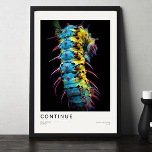 May include: A framed print featuring a vibrant caterpillar with blue, yellow, and red markings against a black background. The print includes the word "CONTINUE" and the phrase "KEEP GOING GENTLY" in white text. A black vase and candle are in the foreground.