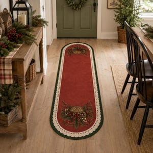 Könnte beinhalten: Ein ovaler Läufer mit tiefroter Mitte, dunkelgrünem Rand und cremefarbenem, gebogtem Abschluss. Der Teppich ist an beiden Enden mit festlichen botanischen Motiven verziert, die Tannenzweige, Tannenzapfen und rote Beeren darstellen.