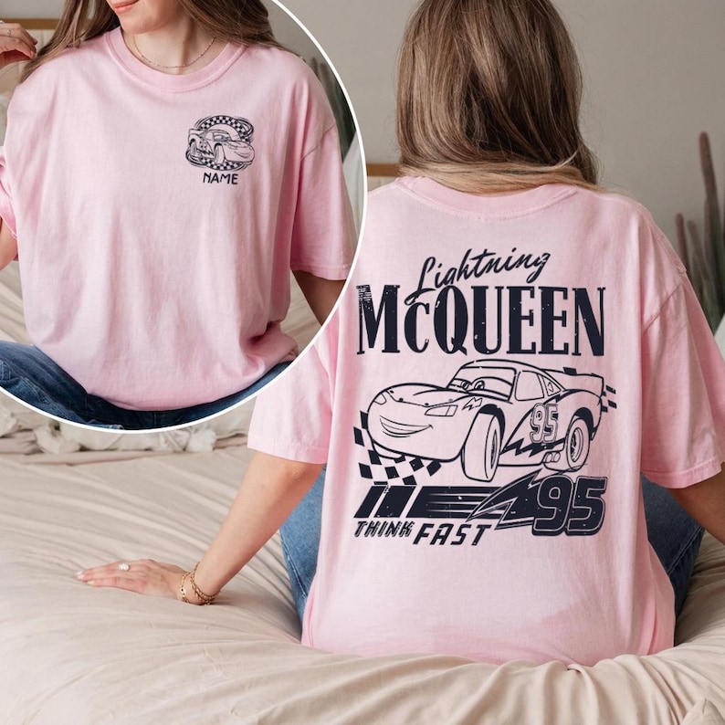 Pu&ograve; includere: T-shirt rosa chiaro con un disegno di auto a cartoni animati. Il retro presenta il testo "Lightning McQueen" e una grafica di auto, con "Think Fast" sotto. Il davanti ha una grafica di auto pi&ugrave; piccola e la parola "NAME".