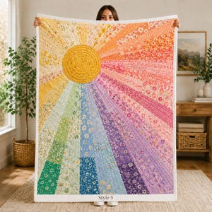 Op de afbeelding: Een rechthoekige quilt met een centrale gele zon en uitstralende banen in een kleurenspectrum van geel, groen, blauw, paars, roze en oranje. De quilt is versierd met diverse bloemmotieven en bevat de tekst Style 5.