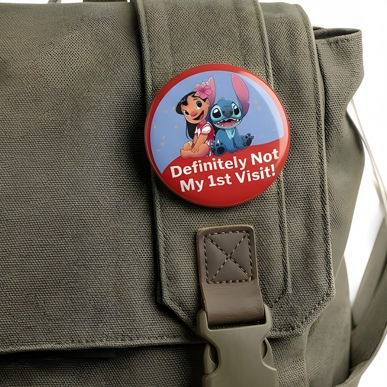 K&ouml;nnte beinhalten: Ein runder Ansteckbutton mit einer Cartoon-Illustration von Lilo und Stitch vor einem blau-roten Hintergrund. Der Text "Definitely Not My 1st Visit!" ist in Wei&szlig; auf dem unteren roten Bereich des Button-Designs aufgedruckt.