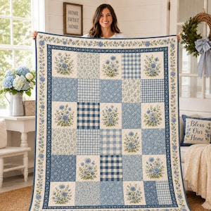 May include: A rectangular patchwork quilt featuring a repeating pattern of blue floral squares and blue and white gingham check squares. The quilt is bordered by a thin strip of blue flowers on a cream background and has a cream-colored edge.