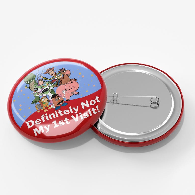 May include: A round pinback button featuring a blue background with Toy Story characters including Woody, Buzz Lightyear, Rex, Hamm, and Mr. Potato Head. The text "Definitely Not My 1st Visit!" is printed in white on a red curved banner at the bottom.
