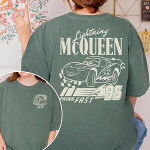Pu&ograve; includere: T-shirt verde con grafica di Saetta McQueen dal film Cars. Il design include il testo "Lightning McQueen", un'illustrazione di auto, il numero "95" e la frase "Think Fast". Una versione pi&ugrave; piccola del design &egrave; sul davanti.