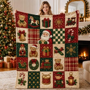 May include: A woven throw blanket featuring a grid of festive Christmas squares. The pattern includes illustrations of teddy bears, Santa Claus, nutcrackers, wrapped gifts, trains, candy canes, snowflakes, a wreath, a drum, and a lantern.
