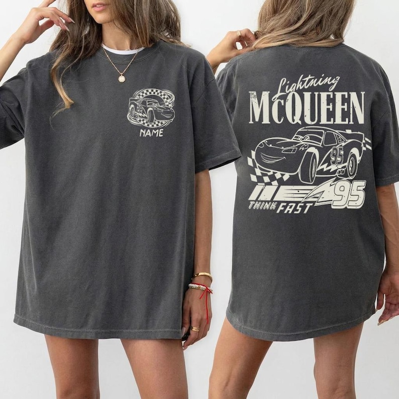 Pu&ograve; includere: T-shirt grigio scuro con un design di auto da corsa a fumetti sul davanti e sul retro. Il design anteriore include un'auto da corsa con la parola "NAME" e il design posteriore presenta "Lightning McQueen" e "95" con le parole "THINK FAST".