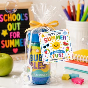 Puede incluir: Un juego de regalo de botella de burbujas con una etiqueta que dice "¡Espero que tu verano sea burbujas de diversión!". La botella es azul y amarilla y dice "Bubbles" y "118,28 ml". El regalo está envuelto en celofán transparente y atado con un lazo amarillo.