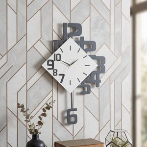 May include: Modern wall clock with a white square face and black hands and numerals. The numerals are stylized and partially surround the clock face. A gray pendulum hangs below the clock face. The clock is mounted on a patterned wall.