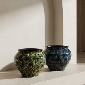 Puede incluir: Dos vasijas de cerámica redondeadas con aberturas anchas y bordes oscuros. La vasija de la izquierda presenta un acabado moteado en verde, amarillo y negro. La de la derecha muestra un patrón moteado en azul profundo, negro y morado con superficie brillante.
