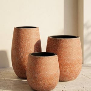 Pode incluir: Três vasos arredondados de alturas variadas com um exterior texturizado na cor terracota, apresentando um padrão claro e craquelado. Cada vaso possui uma borda interna escura e lisa, com uma abertura superior larga e circular.