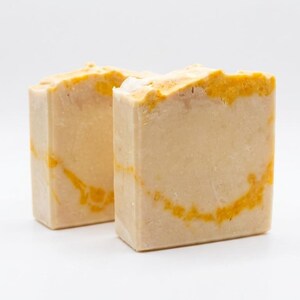 May include: Two rectangular bars of handmade soap. The soap has a light beige base colour with vibrant yellow-orange marbling throughout. The top edges of the soap bars are also accented with the same yellow-orange colour.