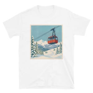 Puede incluir: Camiseta blanca con una ilustraci&oacute;n de estilo retro de un telef&eacute;rico rojo ascendiendo una monta&ntilde;a nevada. El dise&ntilde;o incluye pinos, una pista de esqu&iacute; sinuosa y un cielo azul, evocando un tema de deportes de invierno.