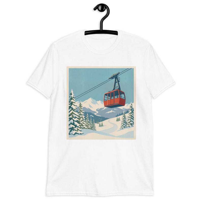 Puede incluir: Camiseta blanca con un dise&ntilde;o gr&aacute;fico cuadrado que representa un telef&eacute;rico rojo sobre un fondo de monta&ntilde;a nevada. El dise&ntilde;o incluye pinos, un cielo azul y una pista de esqu&iacute; sinuosa. La camiseta se muestra en una percha negra.