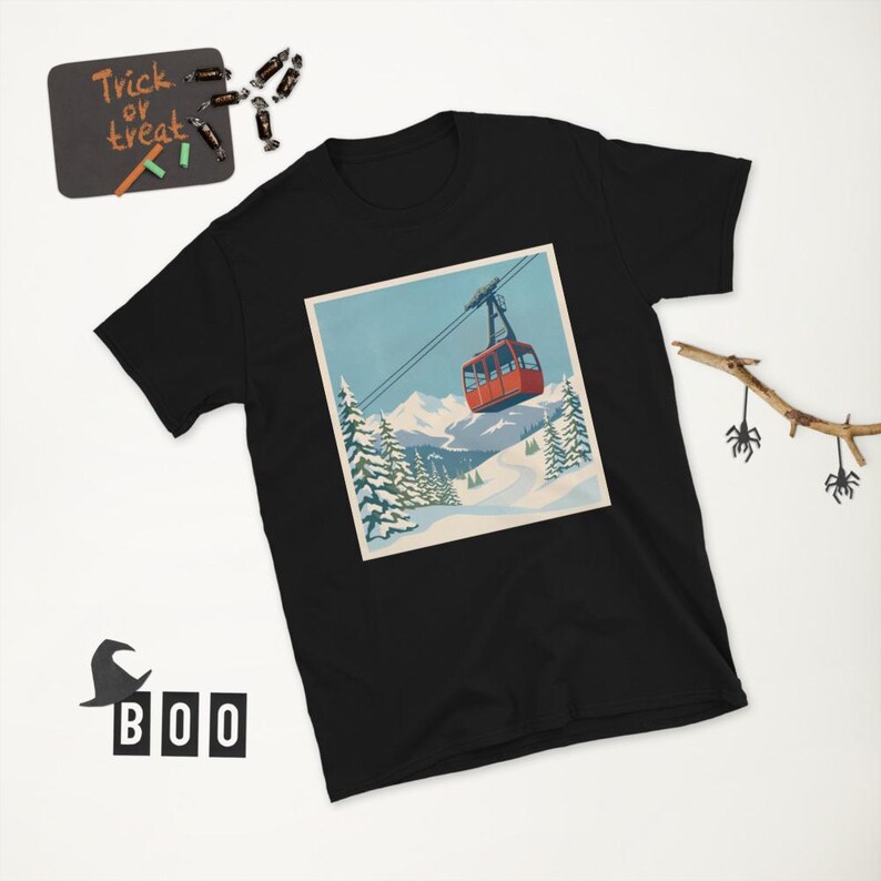 Puede incluir: Camiseta negra con un gr&aacute;fico cuadrado que representa un telef&eacute;rico rojo sobre un fondo de monta&ntilde;as nevadas y cielo azul. La camiseta tiene cuello redondo y mangas cortas. Una peque&ntilde;a pizarra con "Trick or Treat" es visible.