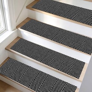 May include: Stair treads with a black and gray chevron pattern are installed on wooden stairs. The treads are rectangular and cover the center of each step. The stairs have white risers and natural wood edges.
