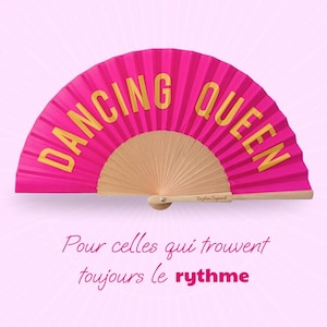 Peut inclure: Un éventail pliant rose vif avec des baleines en bois clair. Le texte DANCING QUEEN est imprimé en grandes lettres capitales dorées sur le tissu. Le manche porte le petit texte En plein Cagnard. Sous l'éventail figure le texte Pour celles qui trouvent toujours le rythme.
