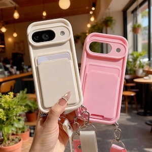 Puede incluir: Dos fundas para teléfono, una blanquecina y otra rosa, cada una con un tarjetero y un recorte para la cámara. Ambas fundas tienen una correa con un cierre metálico. Una persona sostiene la funda blanquecina.