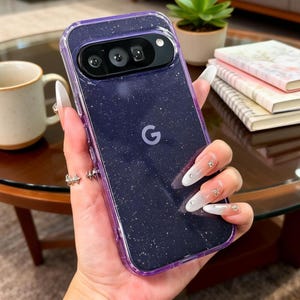 May include: A clear phone case with a purple glitter design. The case has a purple border and a camera cutout. The Google logo is visible on the back of the phone. The phone case is designed for a Pixel 7.