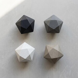 May include: Four geometric polyhedral objects arranged in a square formation. The top left is solid black, the top right is medium gray, the bottom left is white with fine speckles, and the bottom right is a light tan with fine speckles.