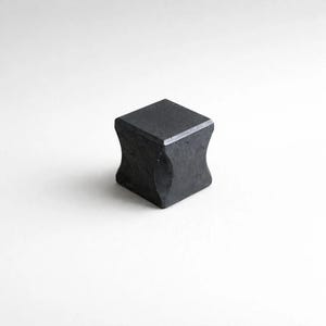 以下が含まれることがあります： 曲線的な側面を持つ、小さく濃い灰色の正方形のキャビネットノブ。ノブは頑丈な素材で作られており、滑らかでマットな仕上がりです。デザインはシンプルでモダンで、さまざまな家具スタイルに適しています。