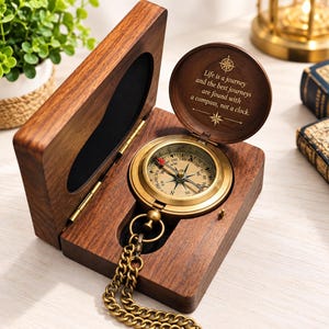 Può includere: Una bussola da tasca in ottone con catena, alloggiata in una scatola di legno scuro. Il coperchio interno presenta il testo inciso: Life is a journey and the best journeys are found with a compass, not a clock. La bussola ha un quadrante circolare.