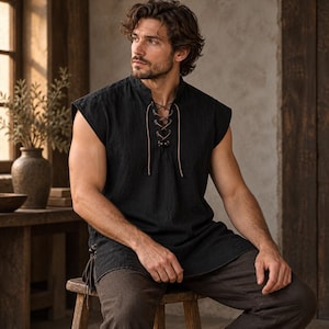 May include: A sleeveless black tunic featuring a stand-up collar and a front lace-up closure with thin brown cords. The garment has a straight hemline and side lacing details at the hips, constructed from a textured fabric with visible weave.