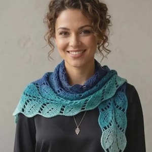 May include: A crochet shawl featuring an ombre color gradient that transitions from deep navy blue at the neckline to a lighter turquoise and pale mint green at the scalloped edges. The accessory has a delicate, openwork leaf-like pattern.