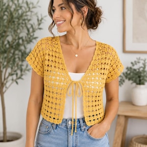 May include: A mustard yellow short-sleeved crochet cardigan featuring an open-front design with a thin tie closure at the center, a V-neckline, and a repeating geometric lace pattern throughout the lightweight knit fabric construction.