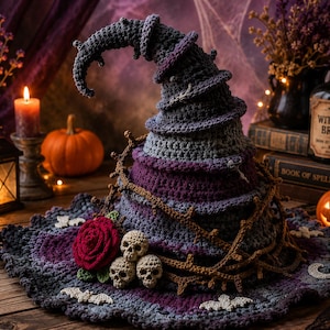 May include: A crocheted witch hat in shades of purple, gray, and black, featuring a curved, pointed top. The hat is decorated with a red crocheted rose, three small beige crocheted skulls, and a brown crocheted vine wrapped around the base.