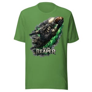 Puede incluir: Una camiseta de manga corta color verde césped con un gráfico de un esqueleto con capucha estirando la mano para atrapar un balón de fútbol americano marrón. El esqueleto está rodeado de humo verde y negro. El texto SLIM REAPER aparece debajo.