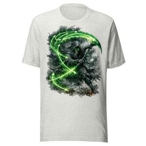 Puede incluir: Una camiseta gris claro de manga corta con un estampado gráfico de una figura encapuchada con un cráneo y ojos de color verde brillante, sosteniendo una guadaña. El diseño incluye flechas verdes giratorias y el texto SLIM REAPER bajo la figura.