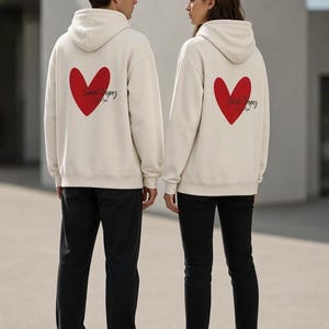 Può includere: Due felpe con cappuccio color bianco sporco con un grande cuore rosso stampato sul retro. La scritta Saint-Tropez è impressa in corsivo nero al centro del cuore. Entrambe le felpe presentano maniche lunghe, un cappuccio e un orlo a coste.