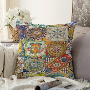 Può includere: Un cuscino quadrato caratterizzato da un vivace design patchwork con motivi di piastrelle in ceramica in stile mediterraneo. La stampa include intricati motivi circolari, composizioni floreali e forme geometriche nei toni del blu, giallo, rosso e verde.