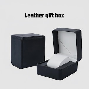 May include: Black leather gift box, open to show a white watch holder. The box is square with a hinged lid and a white interior. The text "Leather gift box" is at the top.