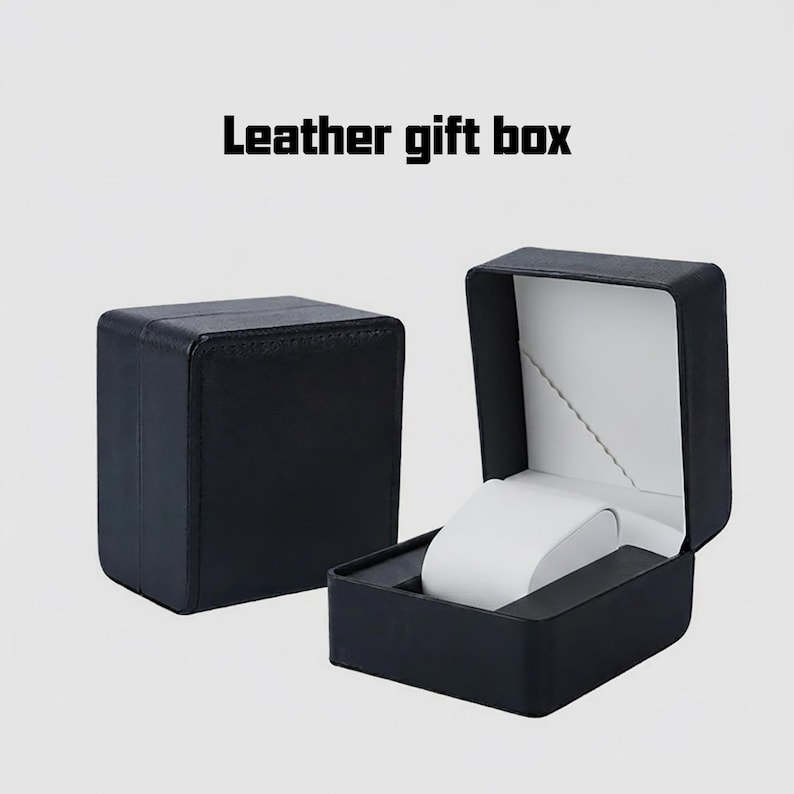 May include: Black leather gift box, open to show a white watch holder. The box is square with a hinged lid and a white interior. The text "Leather gift box" is at the top.