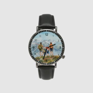 May include: A black wristwatch with a leather band. The watch face features a watercolor painting of a family hiking in the mountains. The watch has a black bezel and silver hands. The watch case is approximately 1.5 inches in diameter.