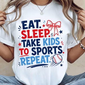 Könnte beinhalten: Weißes T-Shirt mit dem Text "EAT. SLEEP. TAKE KIDS TO SPORTS. REPEAT." in Rot, Blau und Marineblau. Eine rote Schleife und eine Baseball-Grafik sind ebenfalls auf dem Shirt abgebildet. Das Shirt ist ein Freizeitartikel.