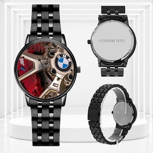 Könnte beinhalten: Eine schwarze Armbanduhr aus Metall mit Gliederarmband. Das Zifferblatt zeigt eine Grafik eines Autorads, eines Bremssattels und des BMW-Logos. Die Rückseite des Gehäuses ist silberfarben und zeigt den Text CUSTOM TEXT für einen personalisierbaren Bereich.