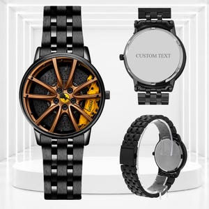 Pode incluir: Um relógio de pulso de metal preto com um mostrador desenhado como uma roda de carro bronze, uma pinça de travão amarela e o logótipo da Ferrari. Inclui uma bracelete de elos pretos, uma tampa traseira com o texto CUSTOM TEXT e uma vista lateral.