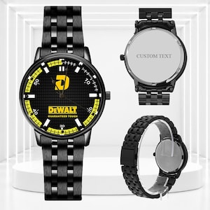 May include: A black metal wristwatch with a textured black dial featuring the yellow DeWalt logo and text "GUARANTEED TOUGH". The watch has a yellow and black minute track, a black link band, and a case back with the text "CUSTOM TEXT".